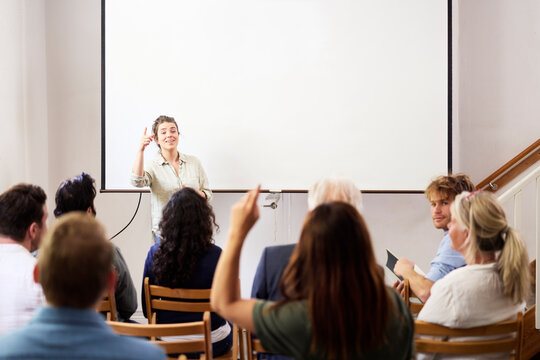 Smiling businesswoman pointing at female colleague while giving presentation to coworkers against blank projection screen in office