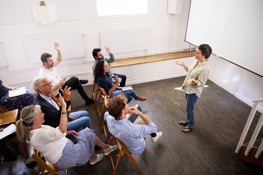 High angle view of businesswoman gesturing while giving presentation to colleagues against blank projection screen at office