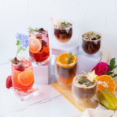 A vibrant arrangement of fresh fruit beverages in various glasses, garnished with herbs and surrounded by colorful flowers.