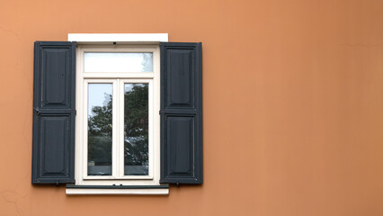 Window with wooden shutters on orange wall. Open shutter window. Exterior view of the building. Copy space.