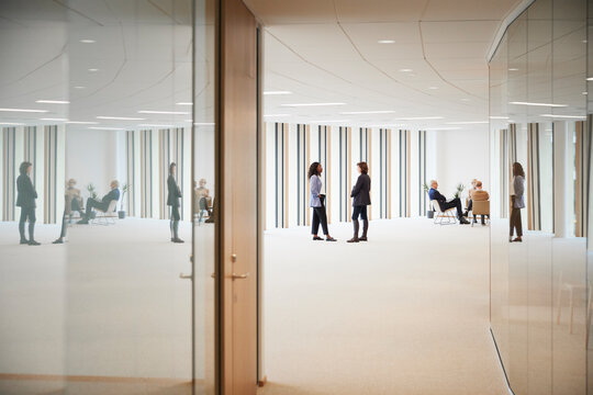 Multiracial businesswomen talking while coworkers sitting in office lobby