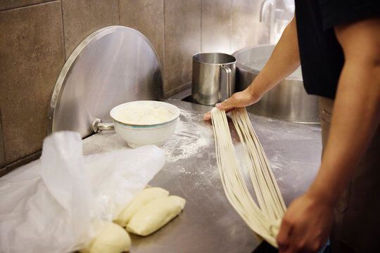 Midsection of chef making noodles on counter in commercial kitchen