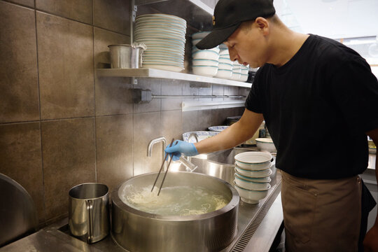 Young chef boiling noodles in commercial kitchen