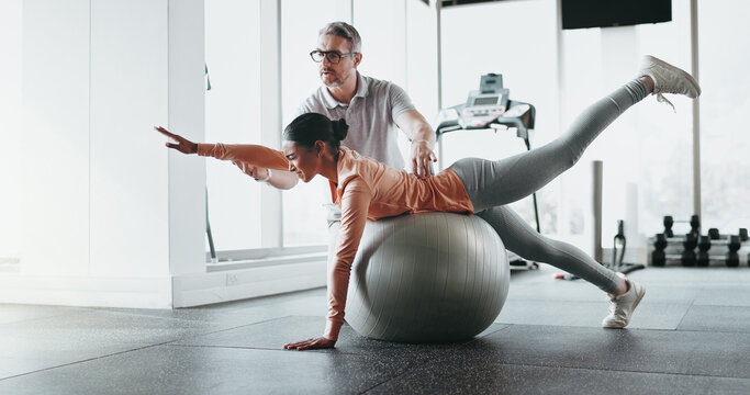 Ball, woman and personal trainer in gym for stretching, rehabilitation and balance training. Man, client and physiotherapy in fitness center for core strength, practice and help in exercise activity - Powered by Adobe