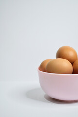 Half view of chicken eggs in the pink bowl isolated on white background. Free space, copy space, empty space on the left side. Potrait photo.