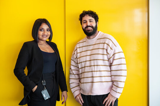 Portrait of businessman and businesswoman standing against yellow cabinet in office