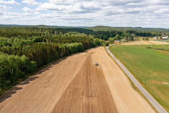 Agricultural field with tractor plowing on land against cloudy sky