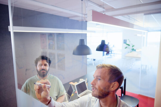 Project manager writing on glass during discussion with colleague in office