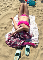 A girl in a swimsuit lies on the sand by the sea