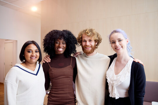 Portrait of diverse male and female business professionals with arms around at office