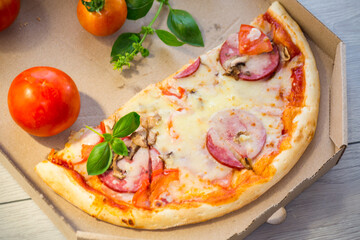 cooked pizza with salami and sausage in a box on a wooden table