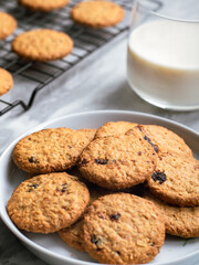 A plate of freshly baked oatmeal raisin cookies garnished with a strawberry, accompanied by a glass of milk and scattered blueberries, set against a light, natural background for a cozy snack scene.