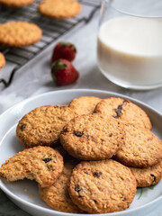 A plate of freshly baked oatmeal raisin cookies garnished with a strawberry, accompanied by a glass of milk and scattered blueberries, set against a light, natural background for a cozy snack scene.