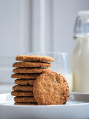 A stack of freshly baked oatmeal raisin cookies neatly arranged on a white plate, with a bottle of milk in the background. The scene is set in a bright kitchen, creating a cozy snack moment.