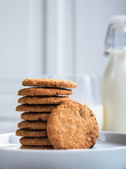 A stack of freshly baked oatmeal raisin cookies neatly arranged on a white plate, with a bottle of milk in the background. The scene is set in a bright kitchen, creating a cozy snack moment.