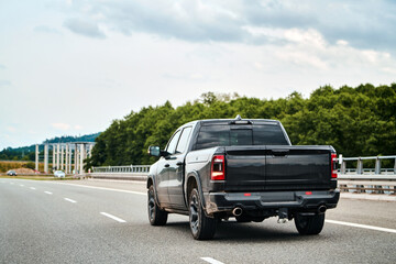 Black pickup truck on a highway with cloudy sky and trees