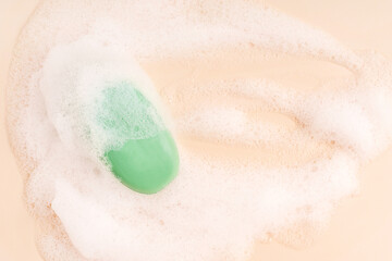 Top view of one scented organic antibacterial soap bar of green colour wet, soapy and covered with white foam bubbles on beige background with copy space used as everyday cosmetics for skin hygiene