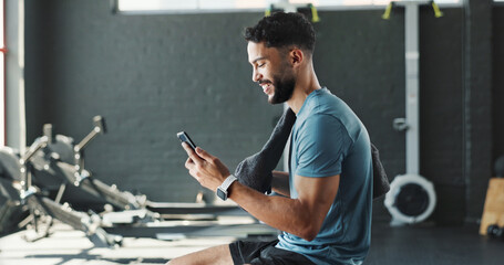 Man, gym and happy with smartphone on rower machine for social media post and interaction. Male person, sports center and profile for fitness with smile or laugh on internet for fun videos or memes © HockleyM3/peopleimages.com