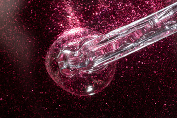macro of cosmetic pipette dropper with liquid gel or face serum on glitter pink background with dramatic light. skin care luxury cosmetics presentation , textures and swatches