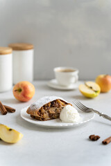 Delicious Freshly baked powdered apple strudel with raisins and ice cream on white plate with red apples and cinnamon on white background. homemade Apfelstrudel. Menu, recipe. Copy space, vertical