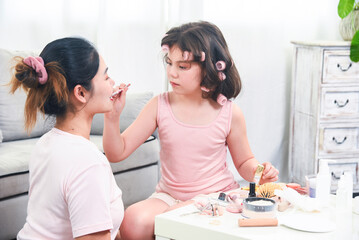 Mother teaches the child to do makeup. Mother and little daughter are doing makeup on each other and having fun.