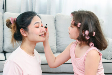 Young Asia mother and little daughter are doing make up for each other and having fun. Family spend time together have a fun in living room with happy holiday concept,happy family.