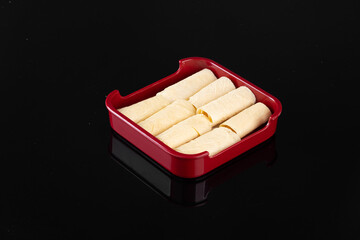 Delicious cheese rolls in a red serving dish on a black background. Perfect snack or appetizer idea for parties and gatherings.