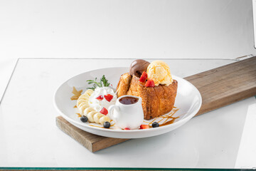 Delicious dessert plate with toast, ice cream, fresh fruit, whipped cream, and syrup on a white background.
