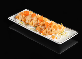 Delicious dumplings served on a white rectangular plate against a black background, garnished with orange topping and shredded vegetables.