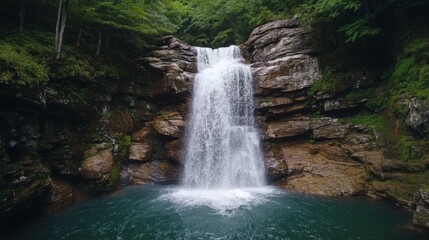Fototapeta premium Majestic waterfall cascading down rocky cliffs into a serene pool, surrounded by lush green forest.