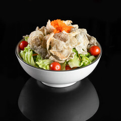 Delicious fresh vegetable salad with cherry tomatoes, lettuce, and crispy toppings in a white bowl on a black background.