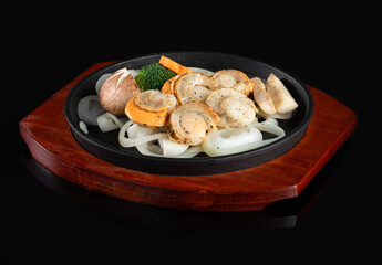 Delicious grilled scallops served on a bed of onions in a black skillet, garnished with herbs, presented on a wooden tray.
