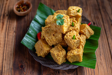 A plate of crispy fried tofu cubes garnished with green chilies and cilantro, served on banana...
