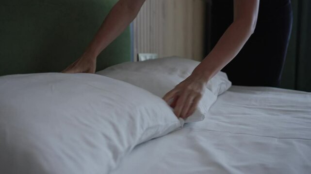 The maid in the hotel changes the bed linen and puts the pillows on the bed. Cleaning service in hotel chains.
