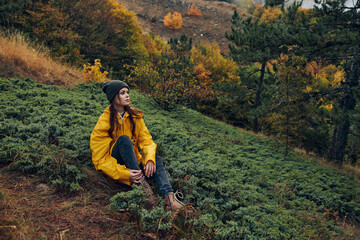 A young woman in a yellow raincoat sitting on a hillside enjoying the fall beauty and tranquility