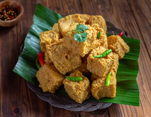 A plate of crispy fried tofu cubes garnished with green chilies and cilantro, served on banana...