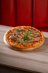 Delicious pizza topped with fresh greens and sliced prosciutto on a wooden board, perfect for a gourmet meal or cozy dinner.