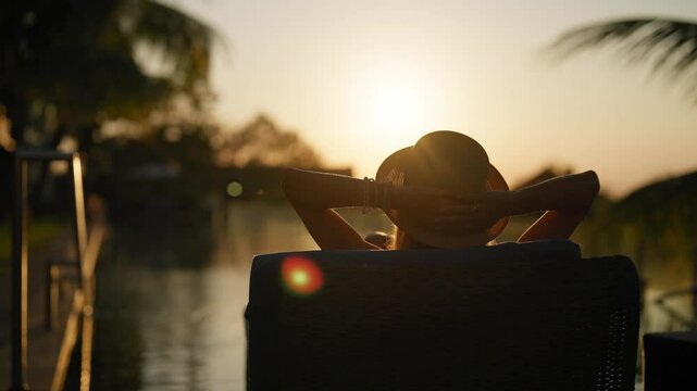 Relax in sunset in summertime, woman lying in lounger in hotel, enjoying view. Summer travel in holidays, recovery energy and vitality, back view of lady in straw hat enjoying relaxation and warm sun