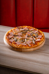 Delicious pizza topped with ham, mushrooms, and cheese on a wooden board in a cozy restaurant setting.