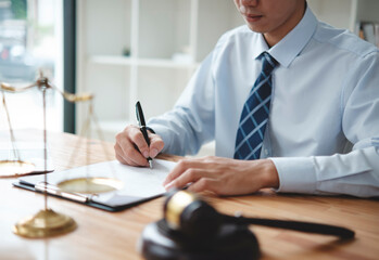 A lawyer in a suit is sitting at his desk, signing legal documents with a gavel on the side.