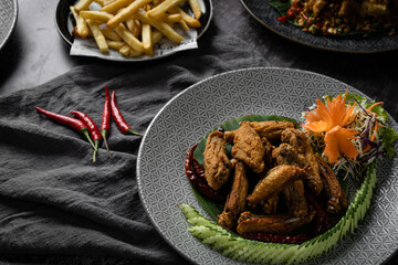 Delicious plate of fried chicken wings served with fresh garnishes and a side of crispy fries on a dark table setting.