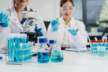 Two female researchers work at a desk in a lab, analyzing liquid samples under a microscope, experimenting with chemistry, and using high technology for important scientific discoveries.