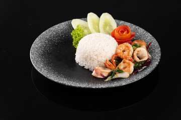 Delicious seafood dish featuring shrimp, squid, and vegetables served with rice on a black plate with a dark background.