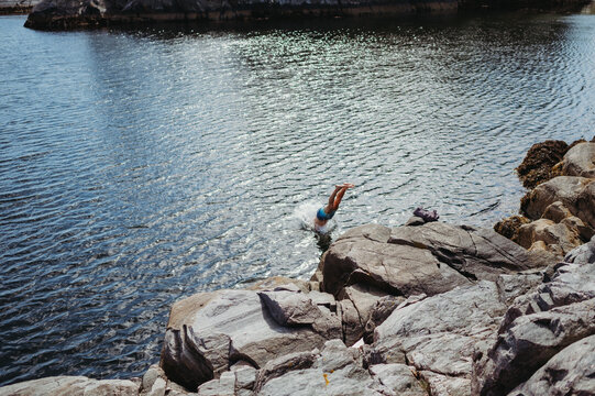 Man diving into ocean from rocky coastline in Flor&oslash;, Norway.