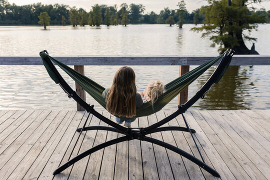 Two people sitting in hammock on dock overlooking lake
