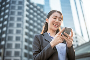 Fototapeta premium Asian young businesswoman using smartphone while standing in the city. 