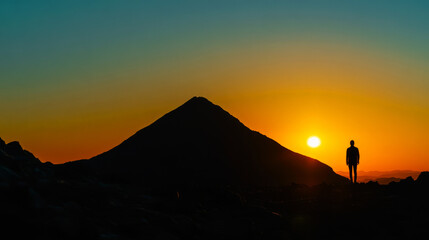 Silhouette Of A Man Standing On A Mountain Peak With The Sun Setting Behind Him.