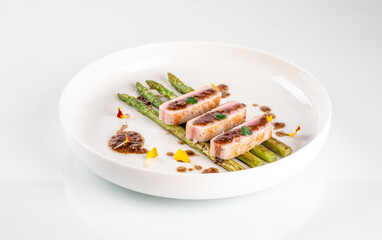 Elegant plate of grilled asparagus with seared tuna slices, garnished with herbs and edible flowers, served in a pristine white bowl.