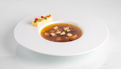 Elegant presentation of clear broth in a white bowl, garnished with colorful toppings and a piece of garnished bread.