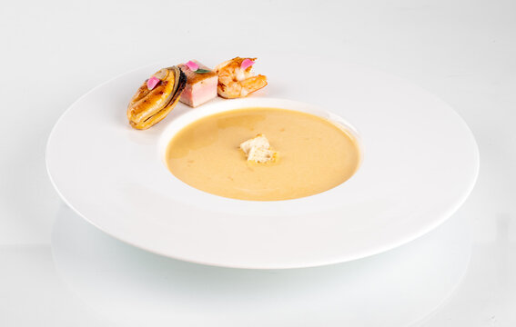 Elegant presentation of creamy vegetable soup garnished with croutons, accompanied by a side of gourmet appetizers on a white plate.